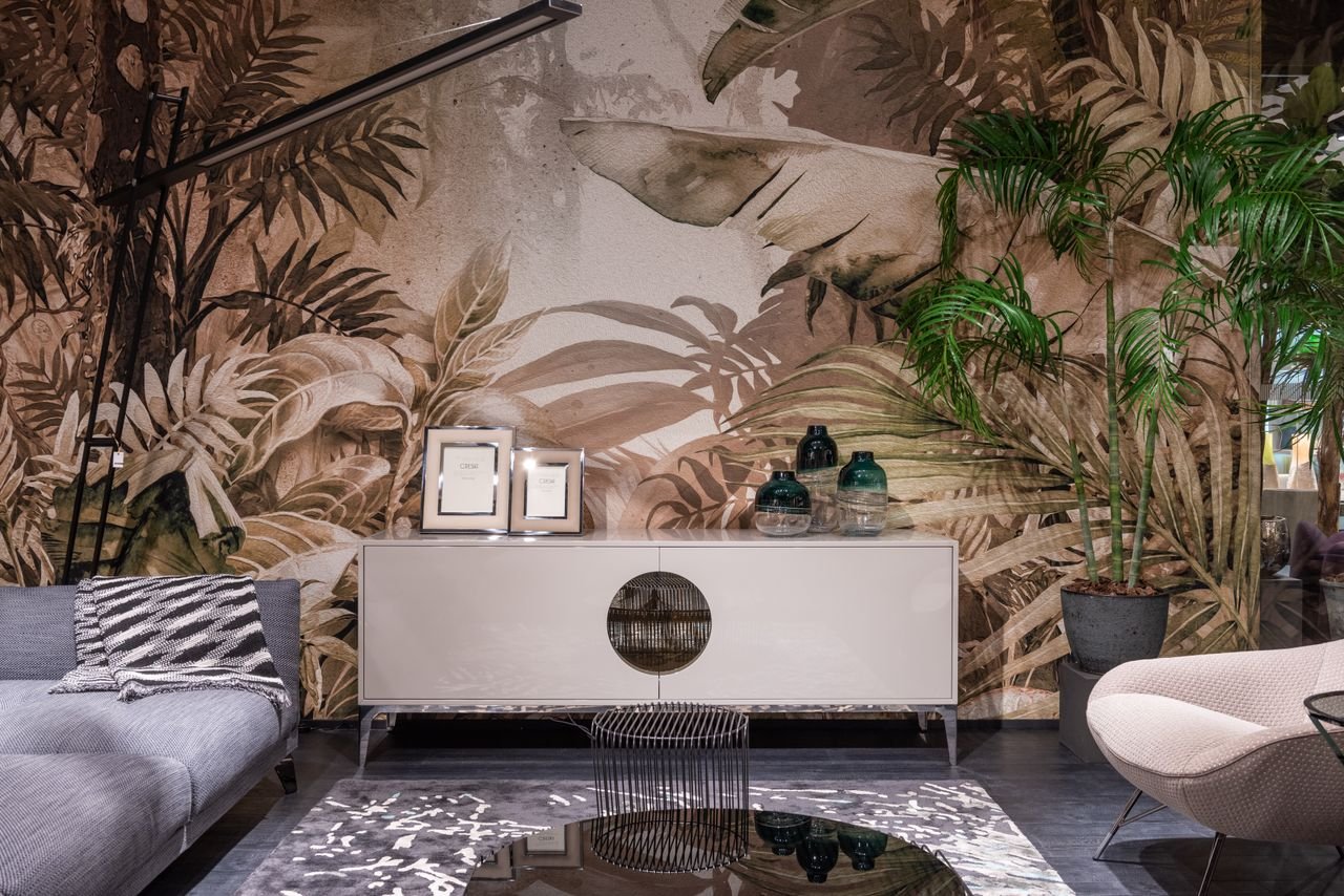Cupboards with decorations placed on rug at painted wall between couch and armchair in contemporary shopping center with green plants